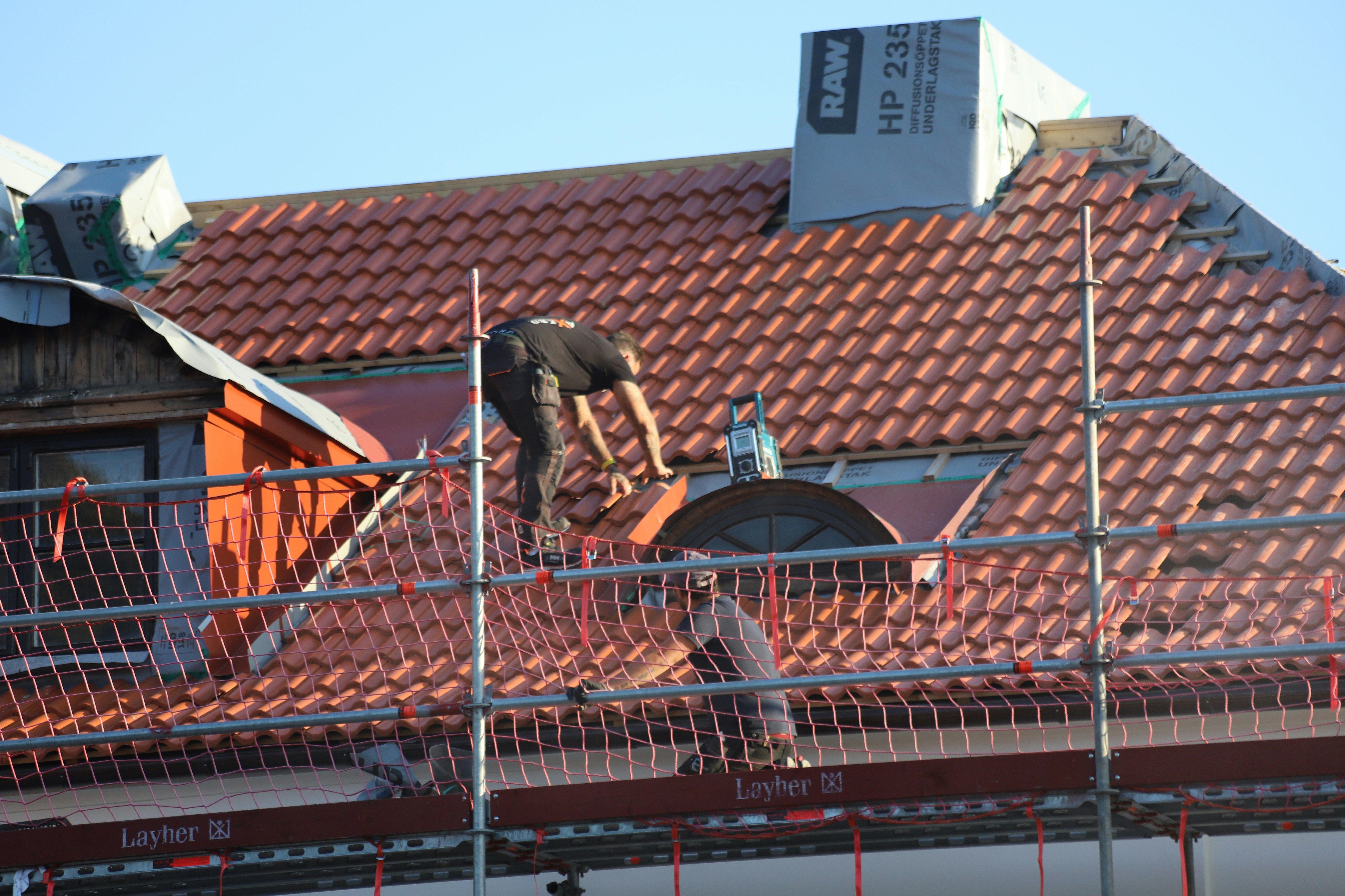 Roofers installing red clay tiles on a steep residential roof